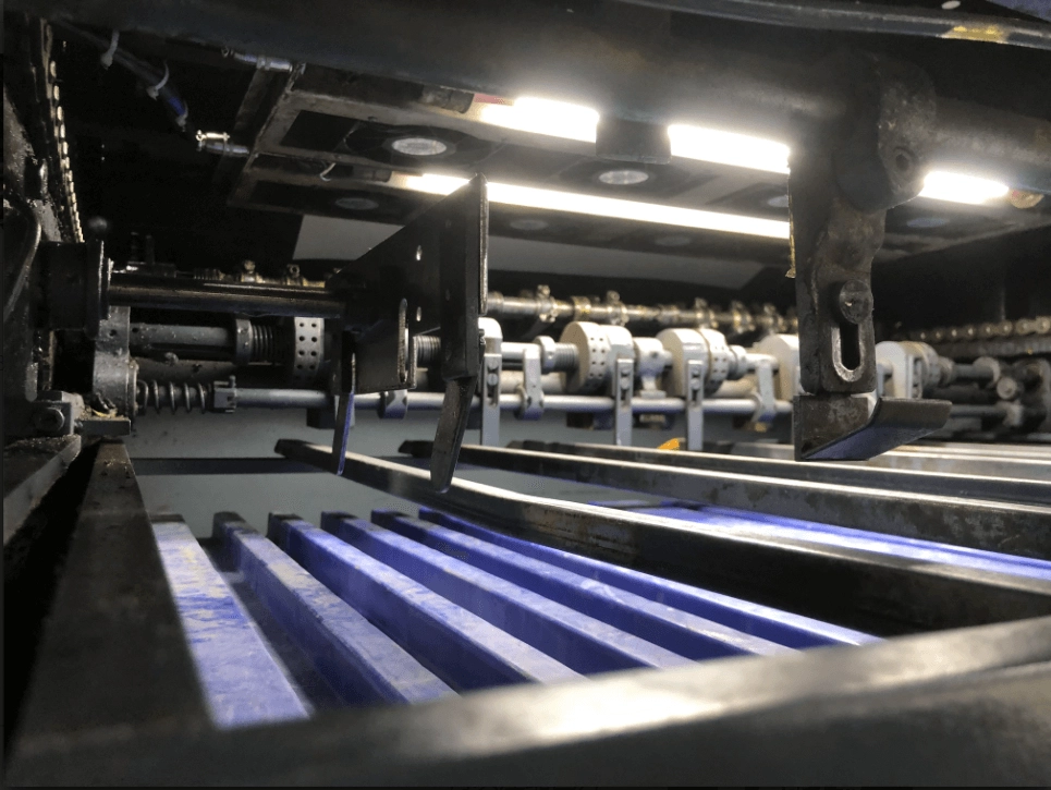 Close-up-view-of-the-interior-mechanism-of-an-industrial-machine,-showing-intricate-metal-parts,-a-series-of-blue-ribbed-components,-and-bright-lights-illuminating-the-machinery. Close-up view of the interior mechanism of an industrial machine, showing intricate metal parts, a series of blue ribbed components, and bright lights illuminating the machinery.