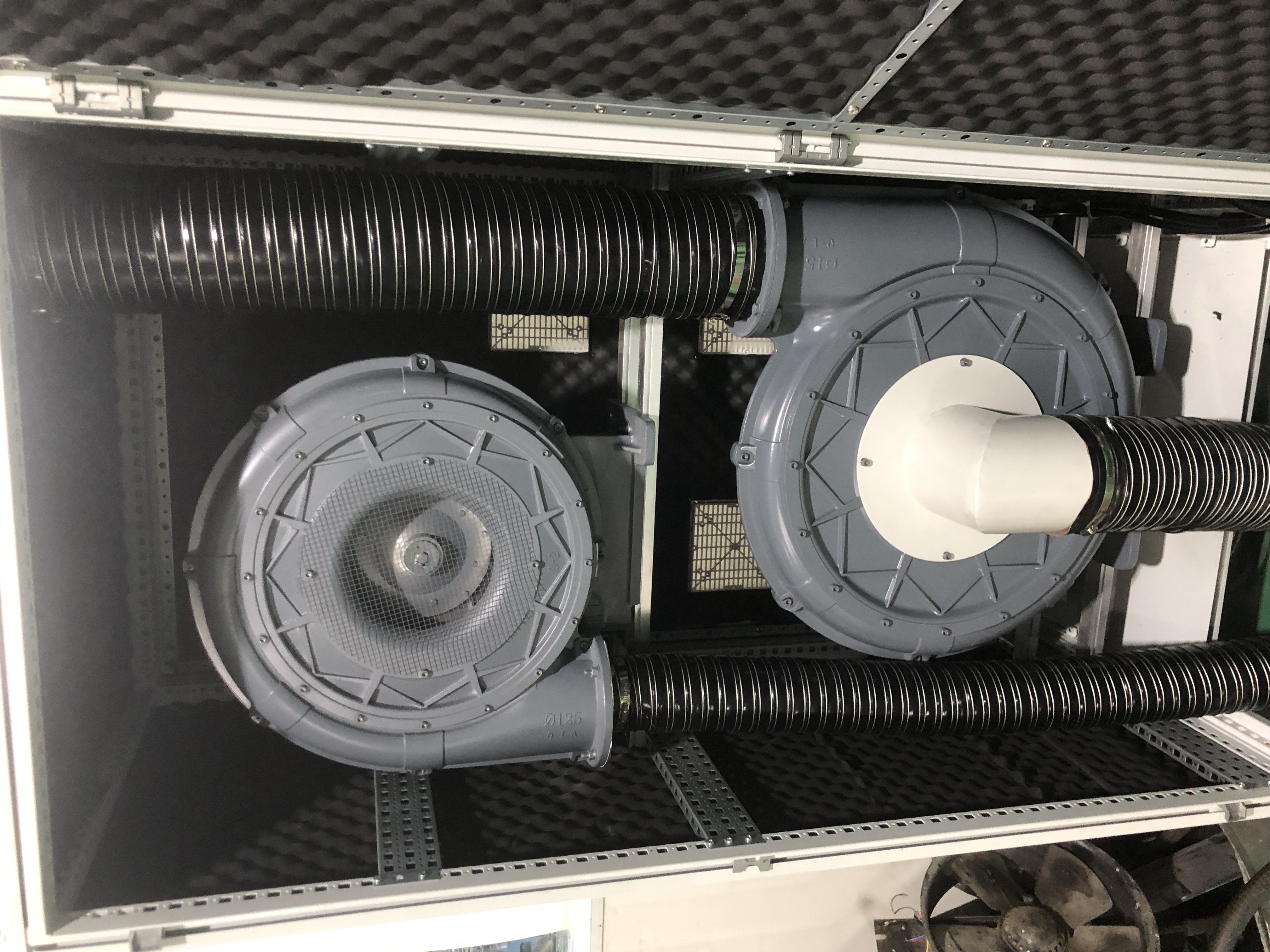 Here's a descriptive alt text for the image:
"Interior view of a soundproofed enclosure containing two industrial blowers with flexible ducting, mounted on a rack system with sound dampening material."